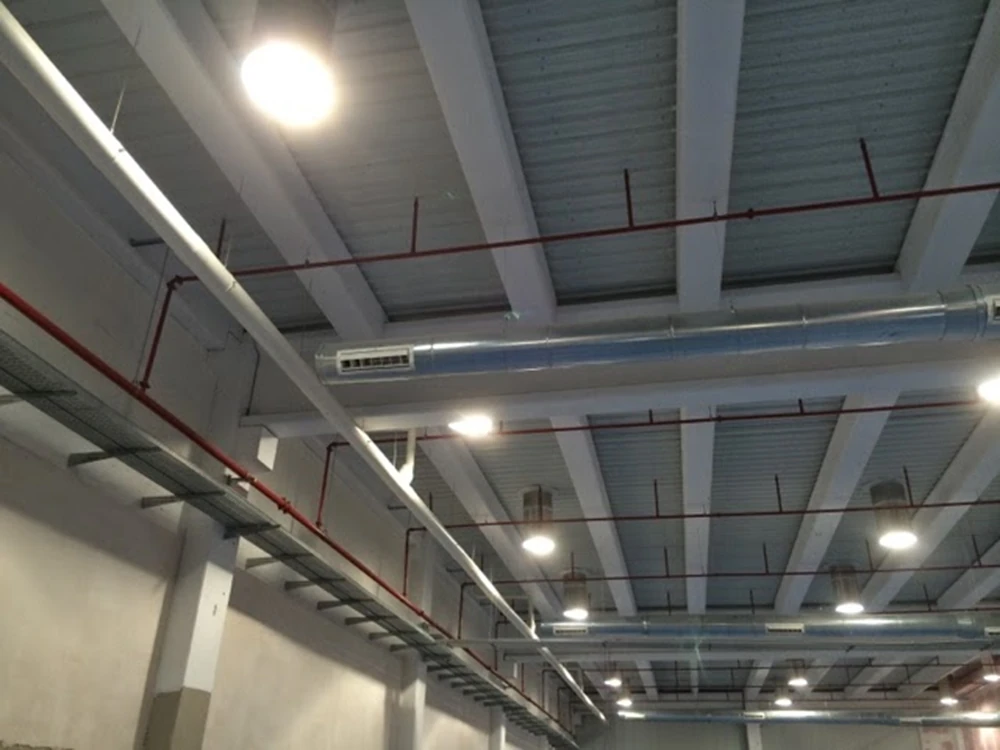 Tuberías rojas y luminarias industriales instaladas en una nave de Sevilla por Extintores A2J, optimizando la luz solar y la seguridad contra incendio